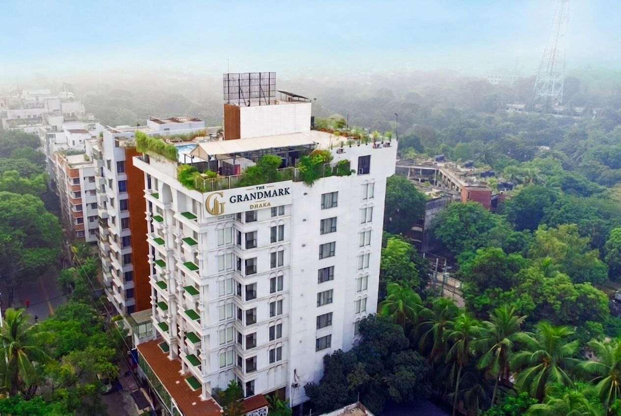 Um hotel moderno com várias varandas, um jardim no terraço e vista para o verde ao redor.