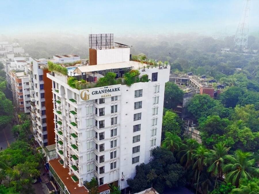 Um hotel moderno com várias varandas, um jardim no terraço e vista para o verde ao redor.