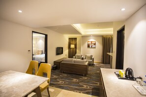 A hotel room with a dining area, a sofa, a TV, and a patterned carpet. - The Grandmark-Dhaka (Dhaka)