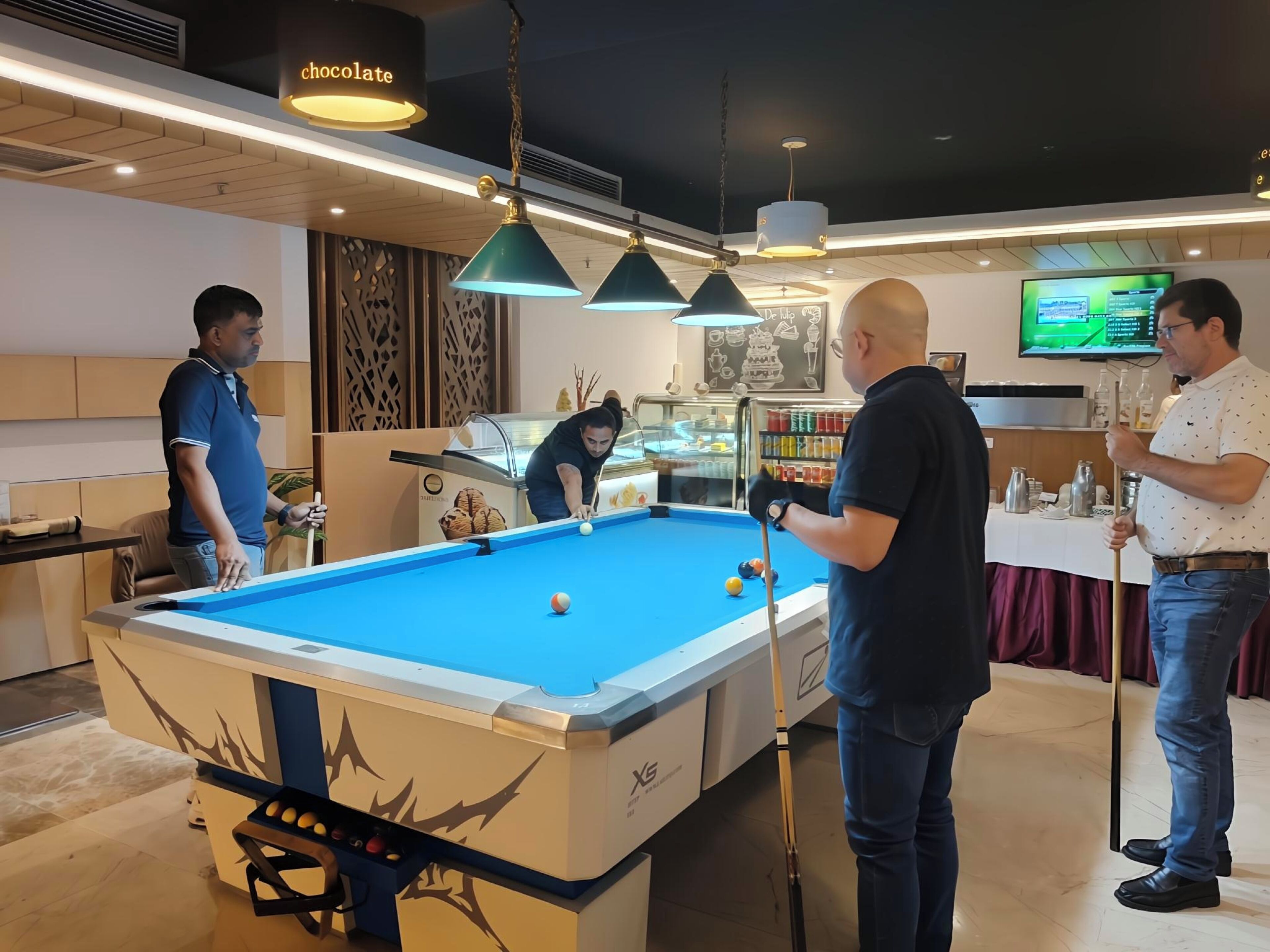 Ein Billardtisch in einem modernen Innenraum mit Deckenbeleuchtung und einer Snackbar im Hintergrund.