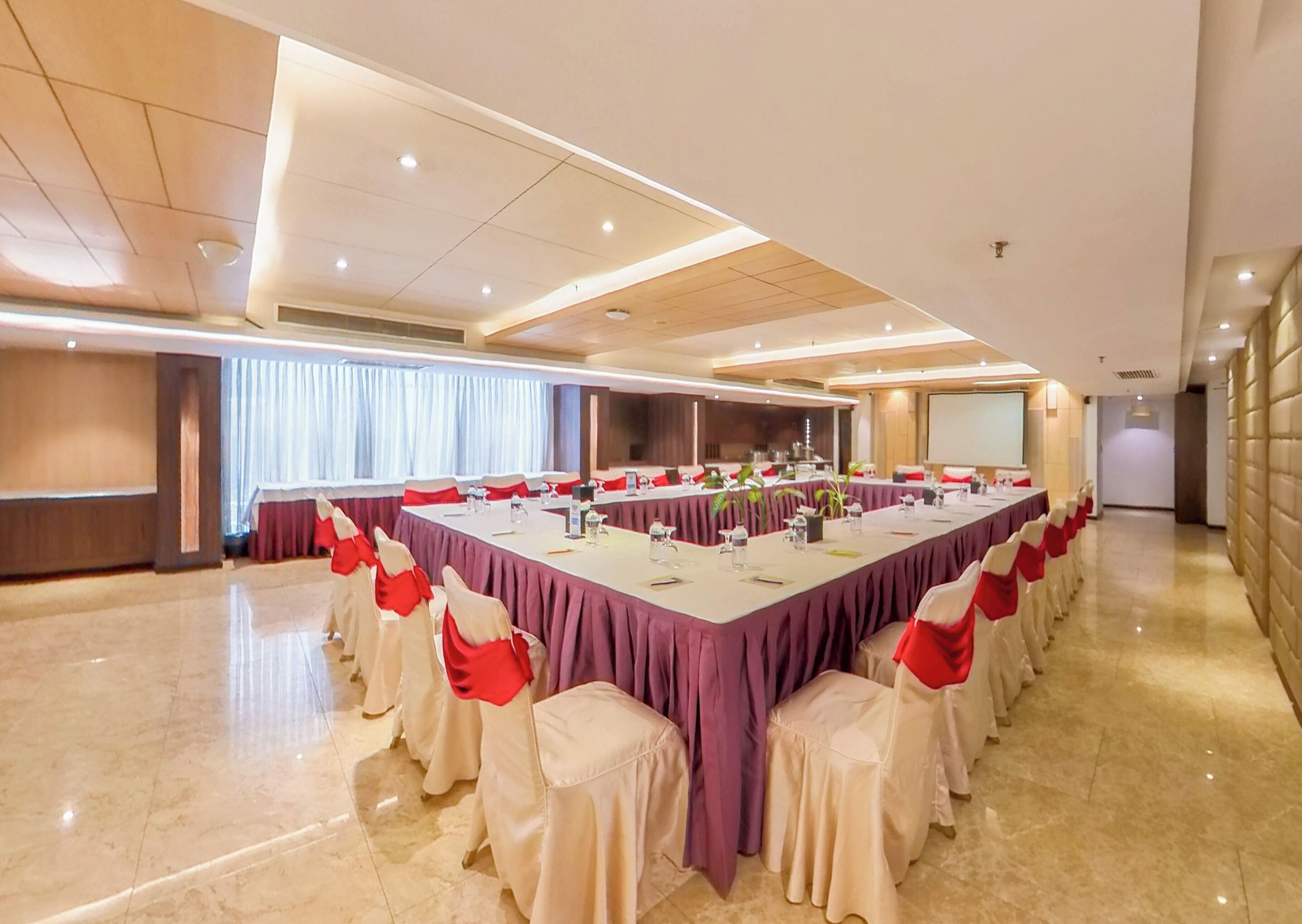 Un salón de conferencias con una larga mesa, sillas y una pantalla de proyector.