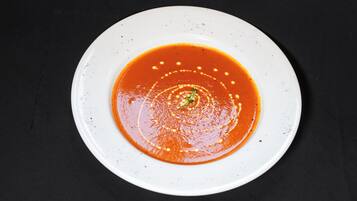 Un plato blanco con sopa roja sobre un fondo oscuro.