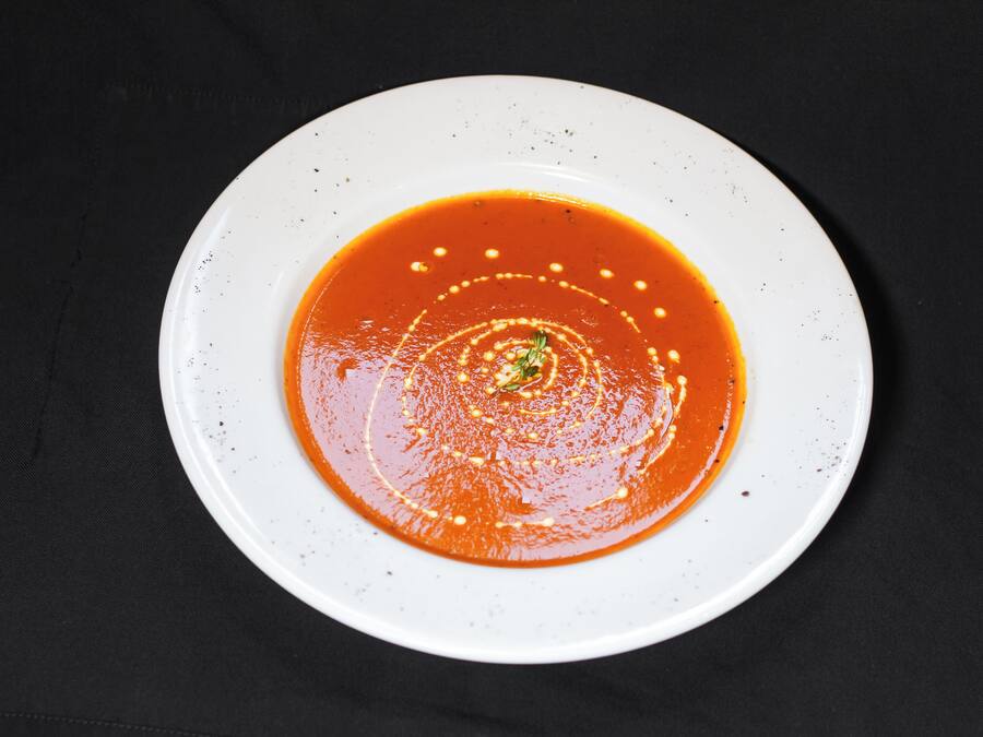 Un plato blanco con sopa roja sobre un fondo oscuro.