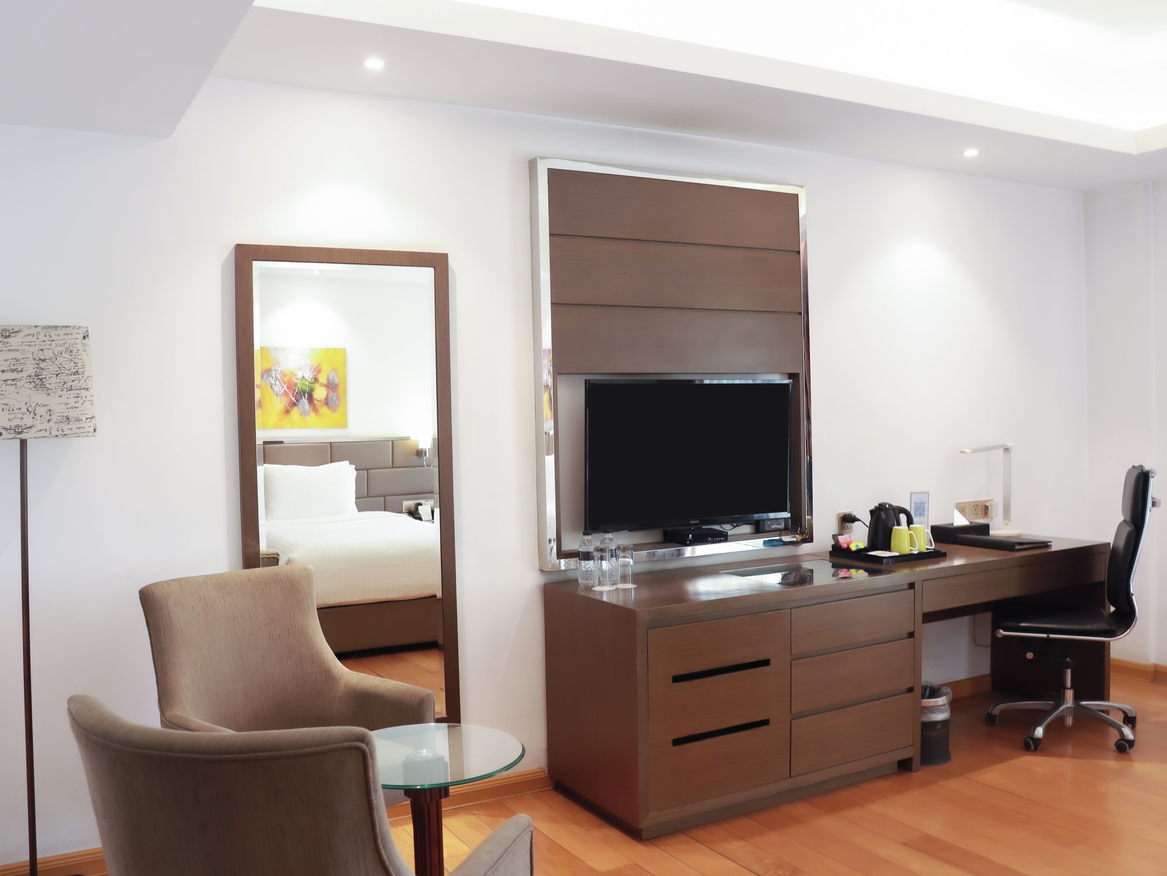 A modern hotel room with a bed, a desk with a computer, a chair, and a television.