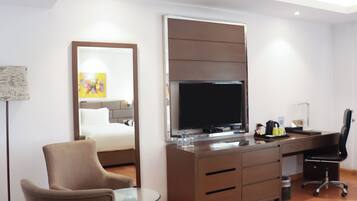 A modern hotel room with a bed, a desk with a computer, a chair, and a television.