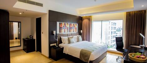 A modern hotel room with a large bed, a desk, a chair, a desk lamp, a nightstand, a mirror, and a window with a view of buildings.