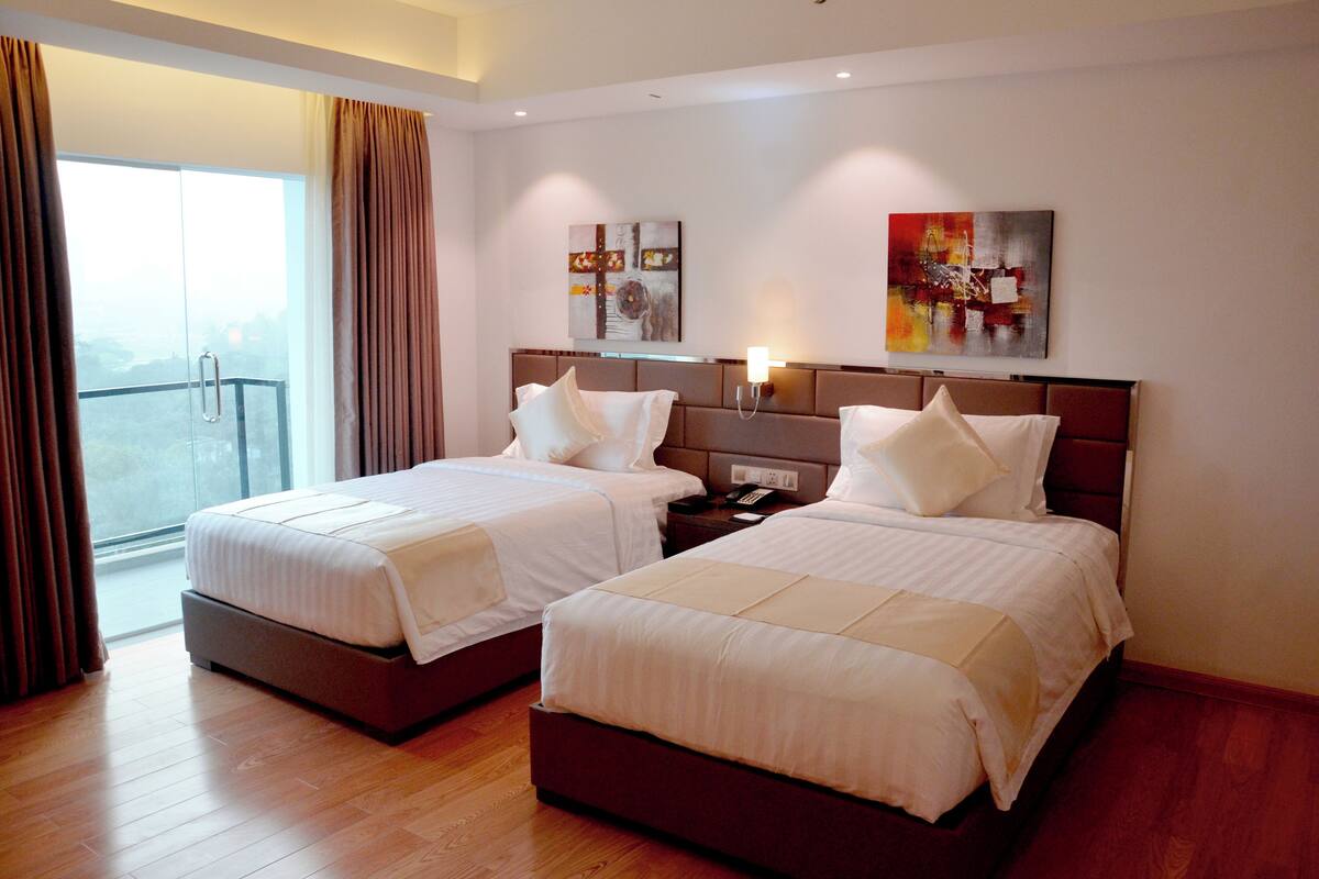 A hotel room with two beds, a balcony, and artwork on the walls.