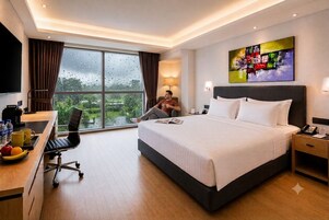 Habitación de hotel con cama, escritorio, silla y un amplio ventanal.