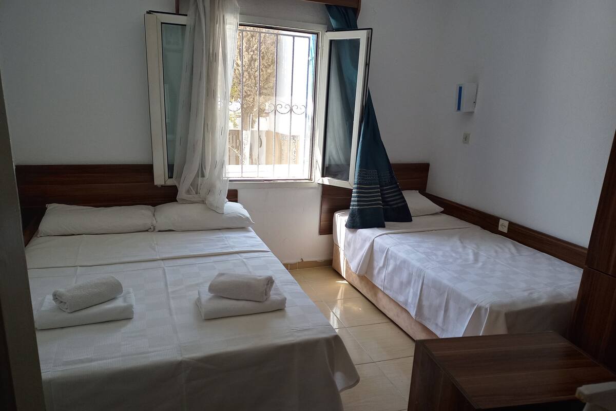 A hotel room with two single beds, a wooden headboard, a window with curtains, and a small wooden table.