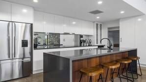 Una cuina moderna amb armaris blancs, un refrigerador d'acer inoxidable, una illa gran amb tamborets i una barra de pedra.