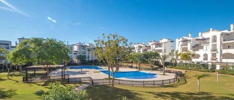 A residential area with a swimming pool, surrounded by greenery and white buildings.