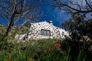 Un bâtiment en pierre doté d’une fenêtre et d’une porte, entouré de verdure et d’arbres.