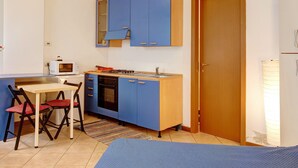 Una cocina compacta con armarios azules, un microondas, una estufa y una zona de comedor con mesa y sillas.