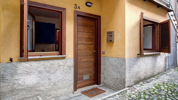Un edificio con puerta de madera, ventana con marco de madera y entrada empaveda con piedra.