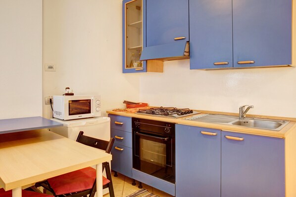 Una cocina compacta equipada con microondas, estufa, horno, pileta y muebles color azul.