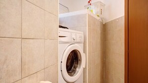 Un lavadero pequeño y moderno con lavadora y secadora integradas, paredes de baldosas color beige y una puerta de madera.
