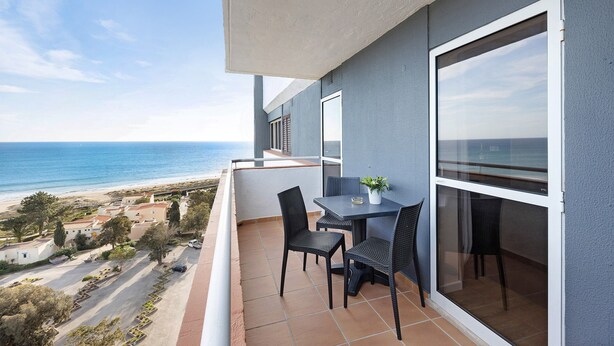 Een balkon met een tafel en stoelen, met uitzicht op een strand en zee.