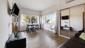 Una sala de estar moderna con sofá, una mesa de comedor con sillas, un televisor montado en la pared y ventanas amplias.