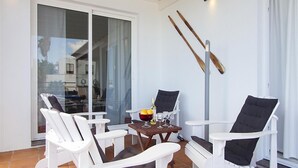 A sunlit patio with white chairs, a table with drinks, and a view through a glass door. - Vacation Villa 'Benedicte' with Sea View, Wi-Fi and Air Conditioning (Puerto del Carmen)