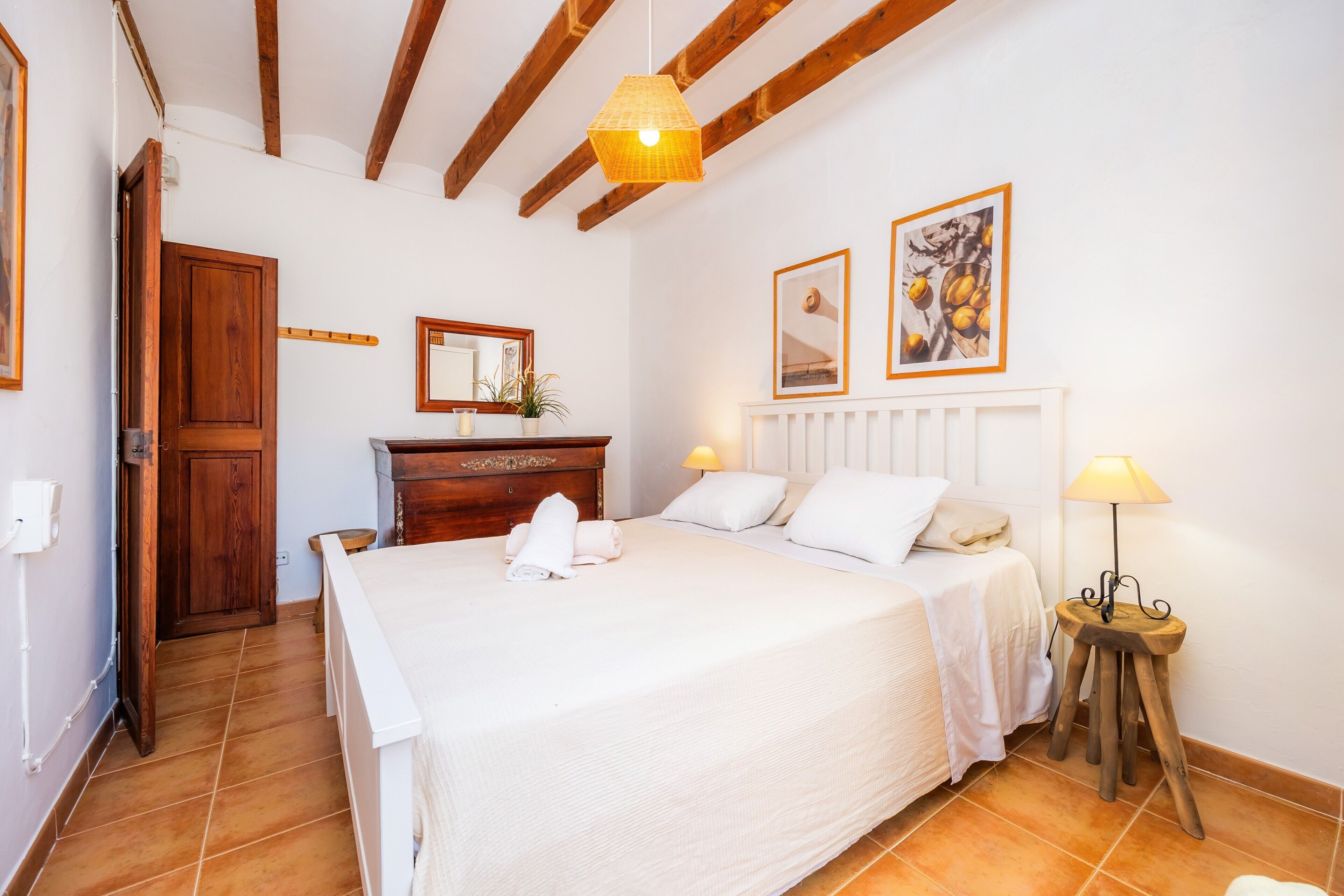 Ein Schlafzimmer mit einem Bett, einer Holzkommode, einem Nachttisch, einer Lampe und zwei gerahmten Bildern an der Wand.