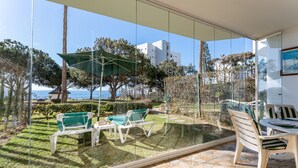 Uma varanda com parede de vidro, área de estar externa e vista para o mar e edifícios.