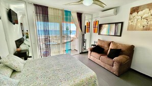 Un dormitorio con cama, sofá, televisión, un cuadro y vista al mar.