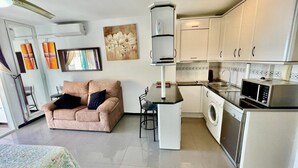 Un espacio habitable compacto con sofá, una pequeña mesa de comedor, lavadora, microondas y fregadero.