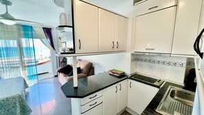 Una cocina compacta con armarios blancos, encimera negra y pileta de acero inoxidable.