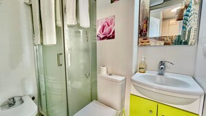 Un baño con cabina de ducha de vidrio, inodoro, lavamanos con espejo y rollo de papel higiénico.
