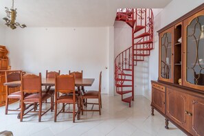 A dining area with a wooden table and chairs, a red spiral staircase, and a wooden cabinet with glass doors. - Holiday Home 'Villa Salvo' with Sea View, Garden & A/C (pachino)