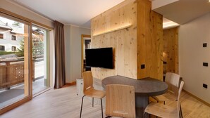 Une chambre moderne dotée d’une grande fenêtre, d’un téléviseur à écran plat fixé sur un mur en bois et d’une table ronde accompagnée de quatre chaises.