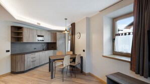 A modern kitchen with a dining area, built-in cabinets, a window with curtains, and a clock on the wall.