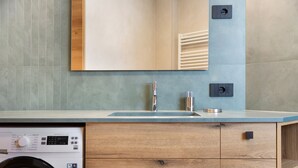 A modern bathroom with a washing machine, a sink with a faucet, and a mirror above the counter.