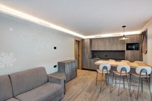 Un salon moderne avec un canapé, un coin repas avec des chaises, une cuisine équipée d’un four à micro-ondes et un buffet en bois.