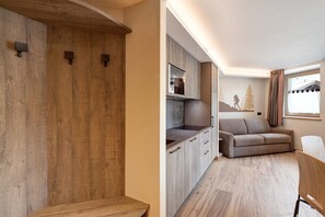 Cocina moderna con armarios de madera, horno empotrado y sofá gris en una sala de estar con ventana.