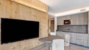 Eine moderne Küche mit Holzschränken, einem an der Wand befestigten Flachbildfernseher und einem Essbereich mit rundem Tisch und Stühlen.