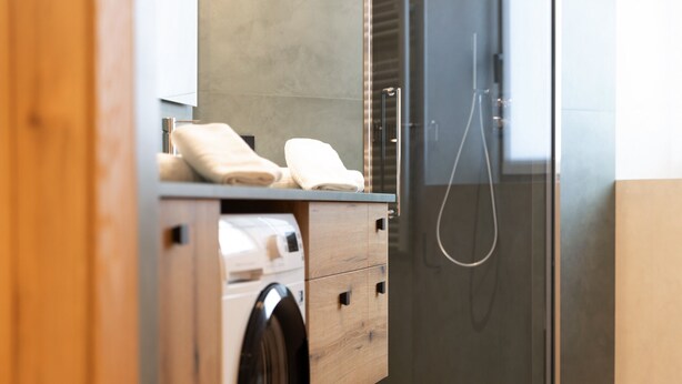 Une salle de bain moderne équipée d’un lave-linge intégré, d’une douche en verre et d’un meuble-lavabo en bois avec des serviettes.