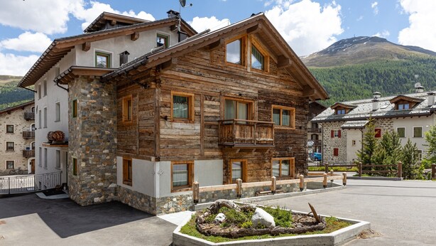 Un bâtiment en bois doté de balcons, de murs en pierre et avec une montagne en arrière-plan.