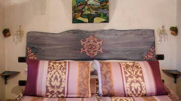 A bed with striped bedding, a decorative headboard, a wall painting, and wall-mounted light fixtures.