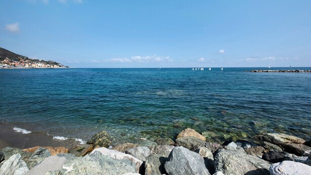 A coastal view with clear water, rocky shoreline, and distant buildings. - Bed and Breakfast 'Gocce Di Cristallo' with Sea View, Wi-Fi and Air Conditioning (Varazze)