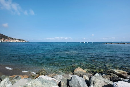A coastal view with clear water, rocky shoreline, and distant buildings.