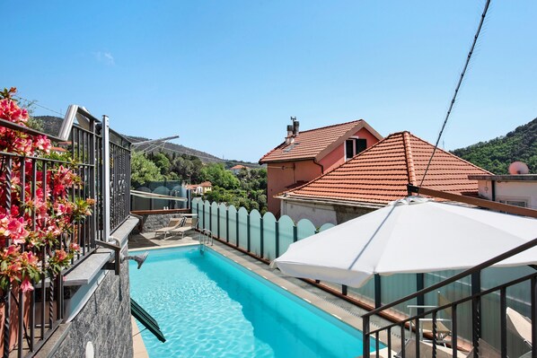 A swimming pool with a clear blue water, surrounded by a white fence, and a red-roofed building in the background.