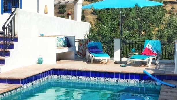 Una piscina con piastrelle blu, due lettini e un ombrellone azzurro.