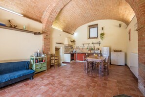 A kitchen with a brick ceiling, a dining table with chairs, a sofa, and a green metal cart with books.
