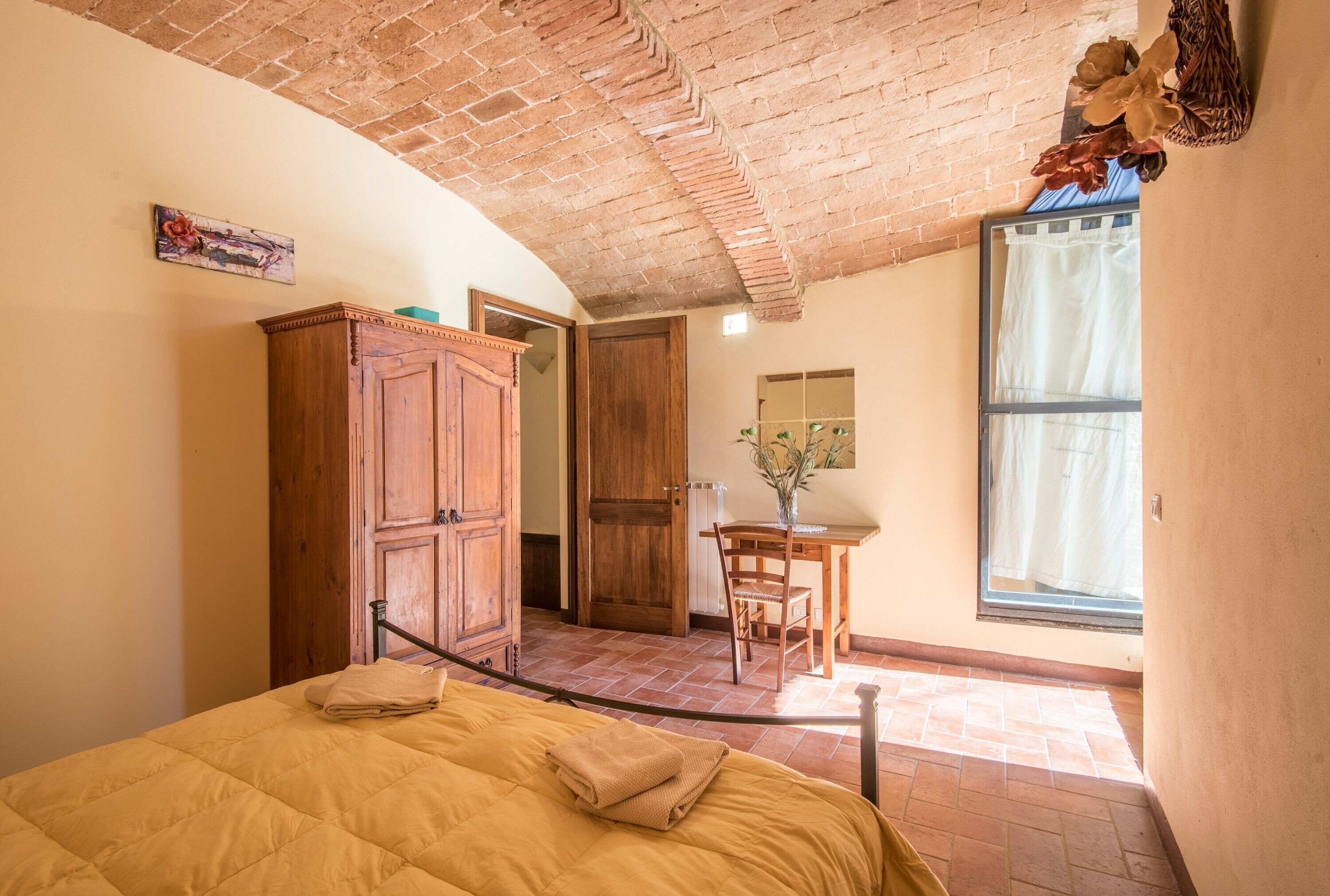 Une chambre à coucher comprenant un lit, une armoire en bois, un bureau avec une chaise et une fenêtre avec des rideaux.