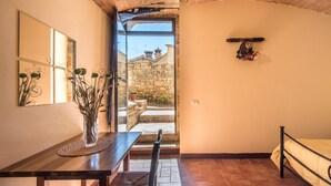 A room with a wooden table, a chair, a bed, a mirror, and a view of a stone building outside. - Holiday Apartment "Arianna" with Terrace & Wi-Fi (Montegabbro)