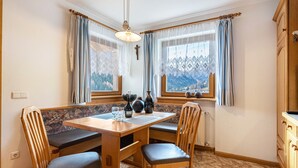 A dining area with a wooden table, chairs, and a view of mountains through the windows. - Holiday Apartment 'Ciasa Alfred' with Mountain View, Wi-Fi & Balcony (La Villa)