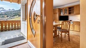 A wooden door leading to a balcony with a view of mountains and a dining area with wooden furniture. - Holiday Apartment 'Ciasa Alfred' with Mountain View, Wi-Fi & Balcony (La Villa)