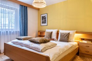 A neatly made bed with pillows, a bedside table with a book, and a framed picture on the wall.