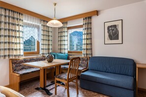 A room with a wooden bench, a sofa, a dining table, and a view of mountains through the window.
